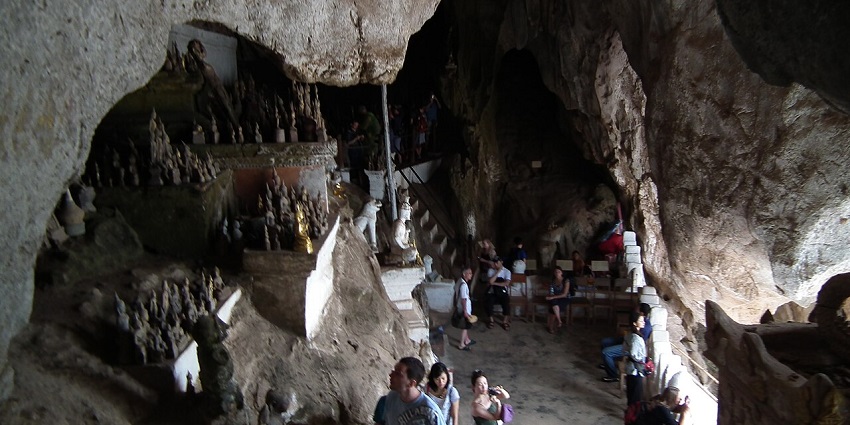 An image of travelers walking deep into the misty corridors of one of the caves in Laos