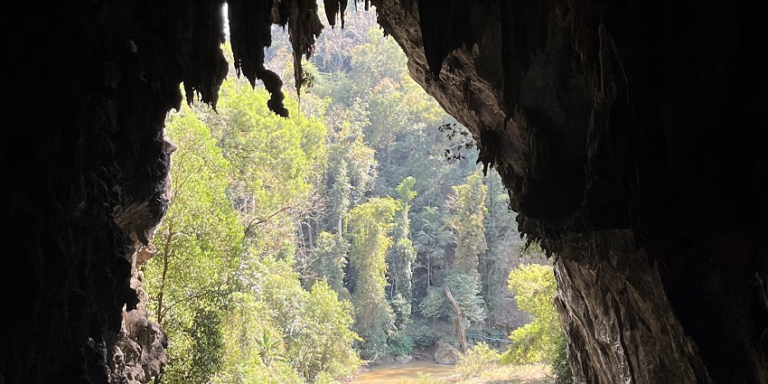 The exit of Tham Lot Cave in Thailand with a river flowing through limestone walls.