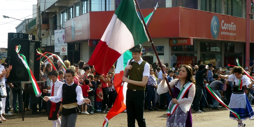 Argentines are performing in the parade wearing traditional attire and holding flags.