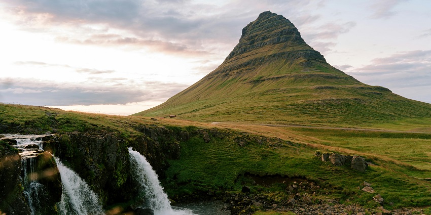 Water gently cascading over moss-covered rocks in a shaded forest during sunset.