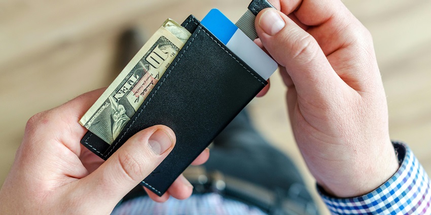 A person wearing a blue checked shirt holding a wallet with money and cards in it.