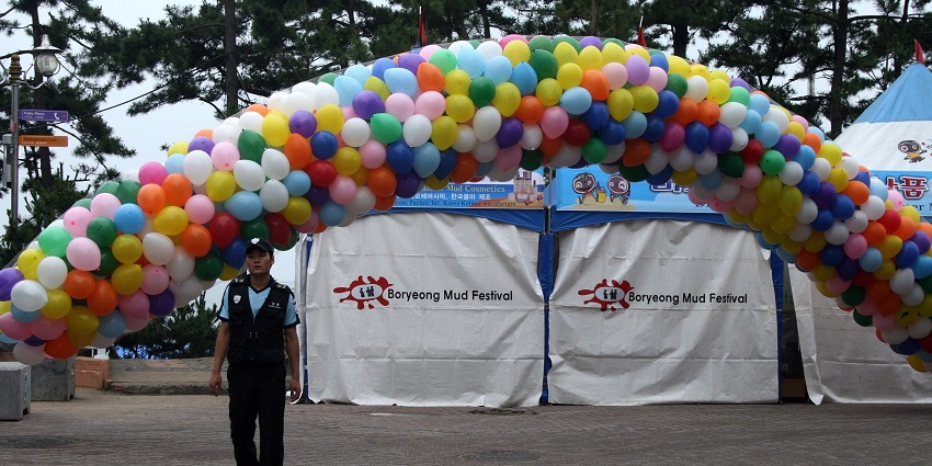 A security guard standing in front of the entrance balloons and multiple tents behind him