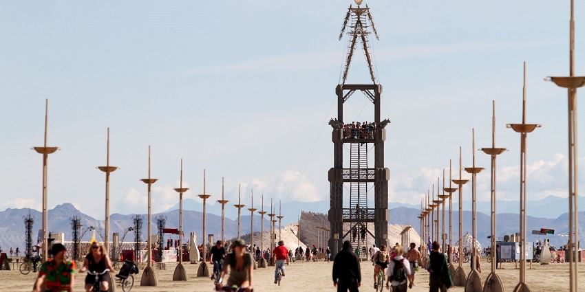 People riding in bikes and some walking towards a huge structure in the Burning Man festival