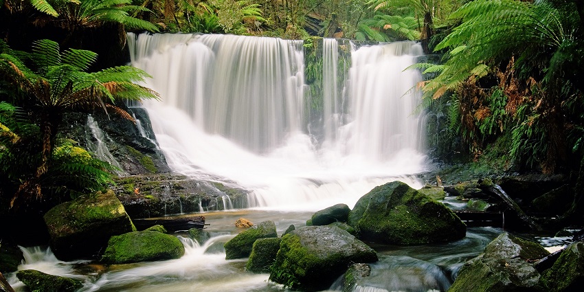 A waterfall flowing through tiered rock formations into a stream passing through big rocks.