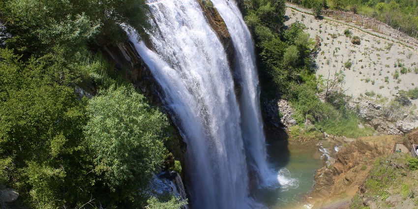 Tortum waterfall from above a cliff with water flowing into the stream, creating a rainbow.
