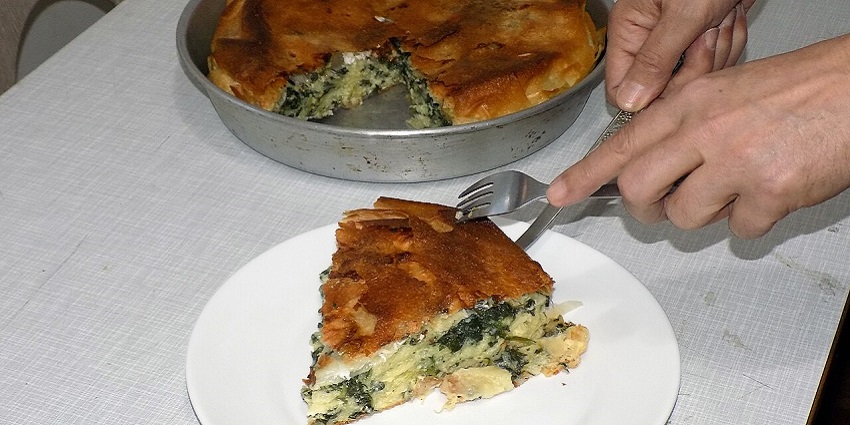 A woman serving a delicious homemade pie of cheese and spinach on a plate with cutlery
