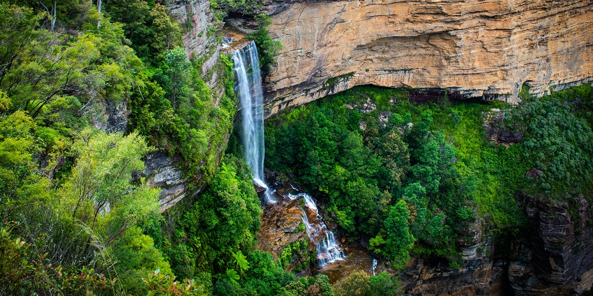 A tall waterfall cascading down a cliff surrounded by lush green forest and rocky walls.