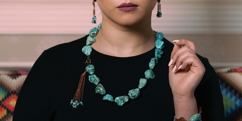 Woman wearing turquoise necklace and bracelet, posing gracefully as soft lighting highlights her stylish gemstone accessories.
