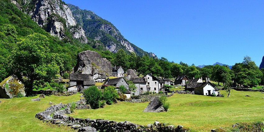 Small village with a few houses near the rocky cliffs partially covered in greenery