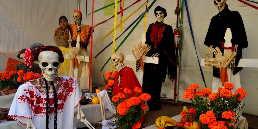 Skeletons in clothes put on the Day of the Dead altar with a woman standing in the corner