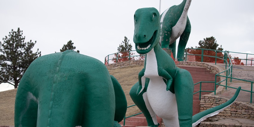 A life-sized model of a Tyrannosaurus rex dominates the outdoor landscape of a dinosaur-themed park, shown in this vivid photograph.