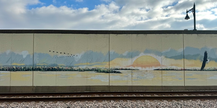 Colorful urban murals are painted along the city walkway, with people passing by.