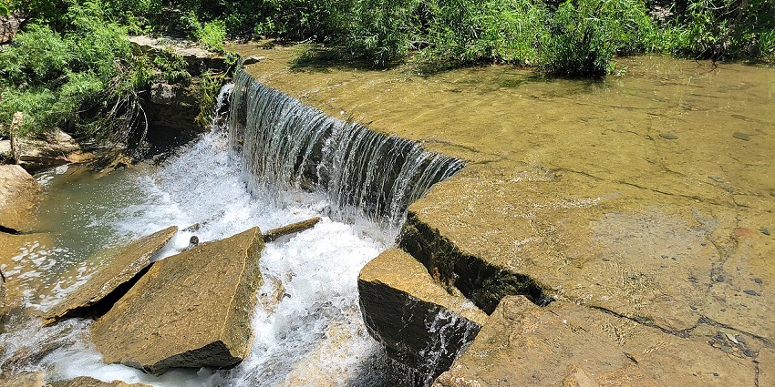 Waterfall flowing into a pool with huge broken stone pieces and trees around the edges