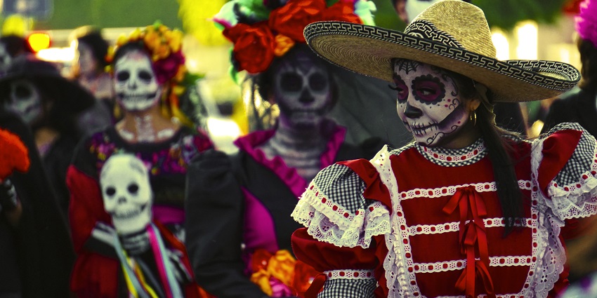 People dressed in gowns and blouses with their faces painted in Day of the Dead parade
