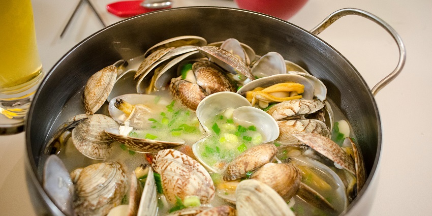 Clams cooked in a pot with vegetables and soup placed on a table with other things