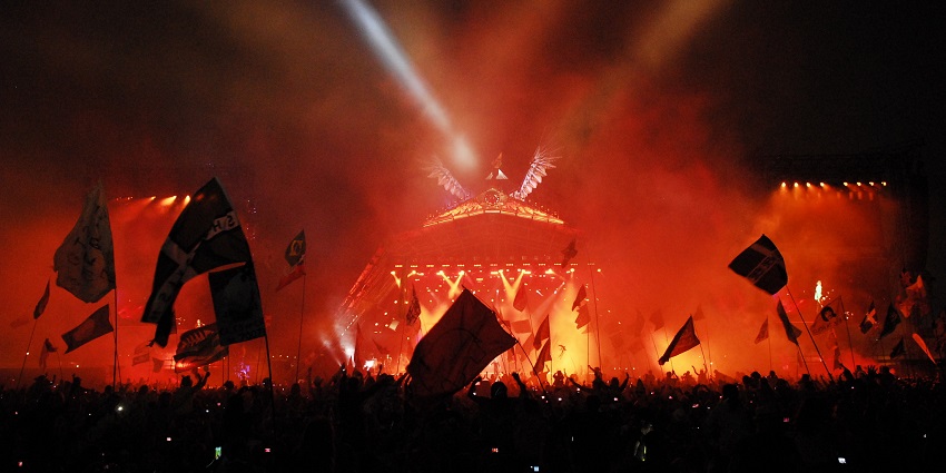 Glastonbury festival with an ongoing concert, red lights and a crowd holding multiple flags