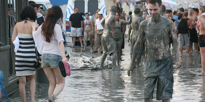 People covered in mud and some clean walking barefoot, carrying their slippers and sandals