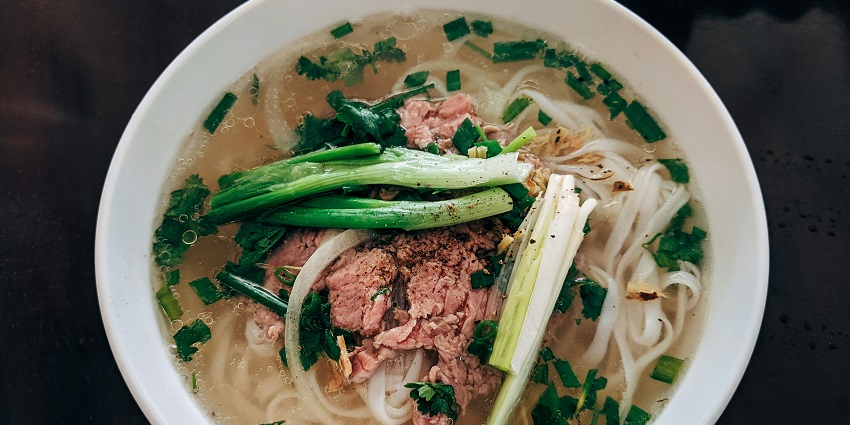 Delicious white noodle soup accompanied by fresh green leaf vegetables in a white bowl