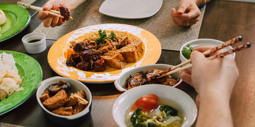 A family-style Asian meal in Hanoi, Vietnam, features tofu, noodles, and vegetables
