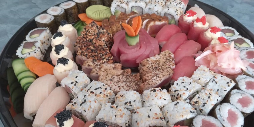 Assorted sushi platter with rolls, sashimi, garnishes, and wasabi, served in a plate