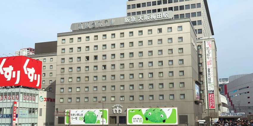 Building of hotel Osaka Shin Hankyu with multiple signages, billboards and people walking