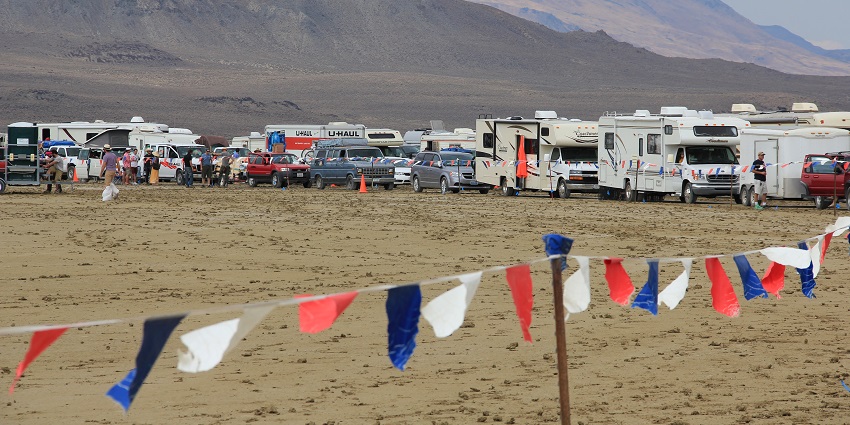 Cars, trucks and RVs lined up in separate spots, people walking around and border flags