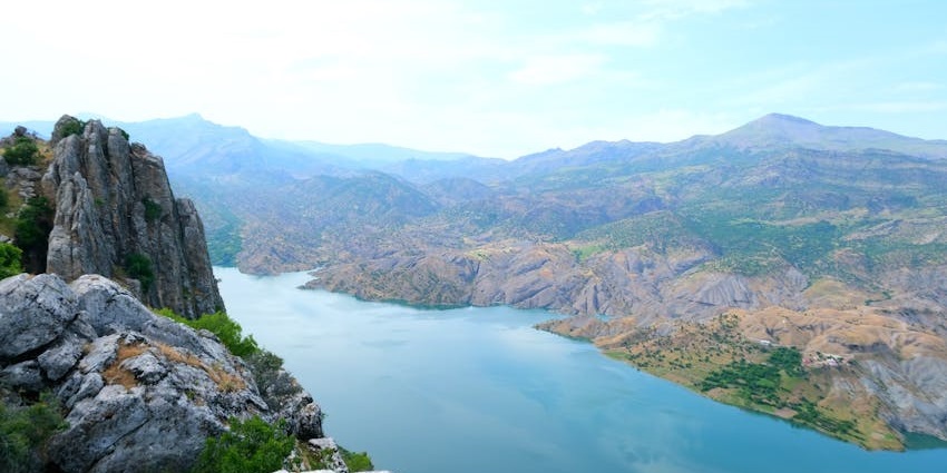 Scenic view of clear blue water surrounded by rugged rocky mountains and open skies.