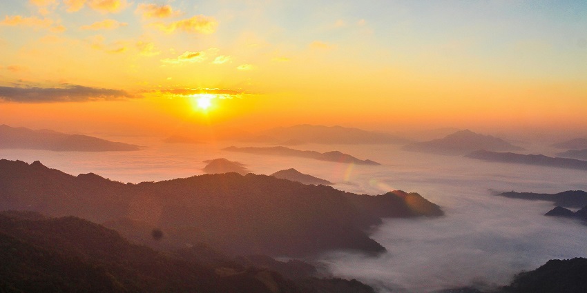 Phu Chi Fa Mountain features a dramatic cliffside peak, lush greenery, and breathtaking clouds blanketing the valleys below at sunrise.