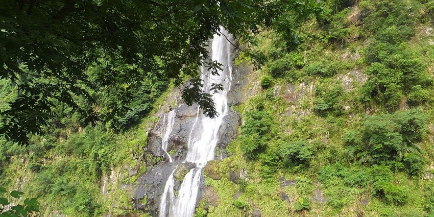 A waterfall rushes through a lush mountain landscape, with mist rising from the water.