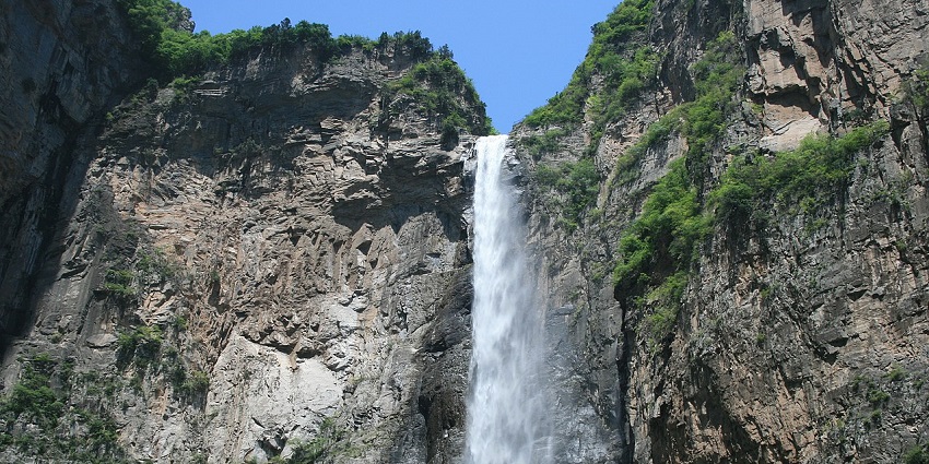 The white ribbon-like water of the Yuntai waterfall falls from lush, green rocky mountains.