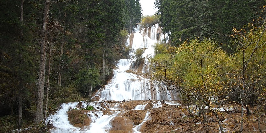 A wide view of Zhaga Waterfall cascades from rocky steps covered with lush greenery.