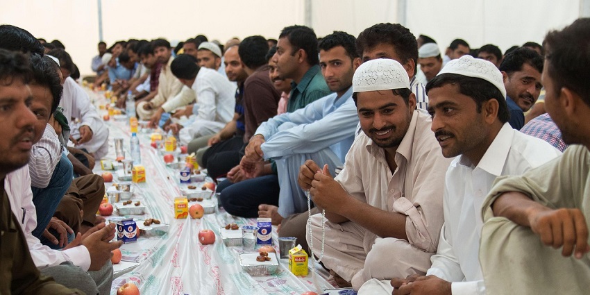 Devotees sit face-to-face and partake in a feast on the floor with a carpet during Iftar