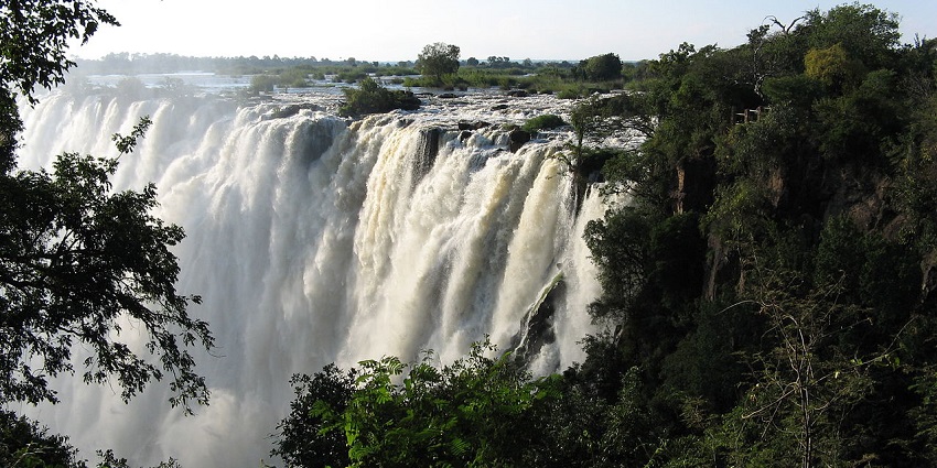 Waterfall dropping from a height, surrounded by lush forest in the foreground and background