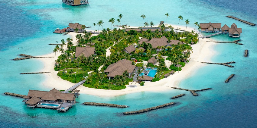 Aerial view of tropical beach with turquoise waters, soft sand, and palm-lined shore.