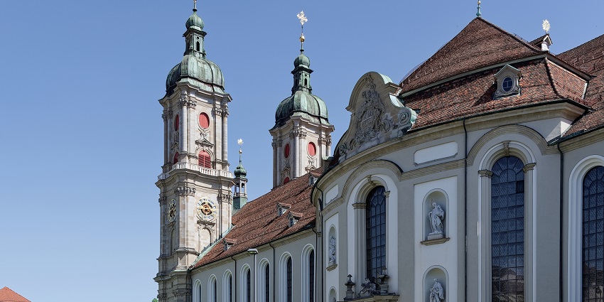 The Abbey of Saint Gall is among the iconic monuments in Switzerland, featuring historic buildings, a large courtyard, and green trees under a blue sky.