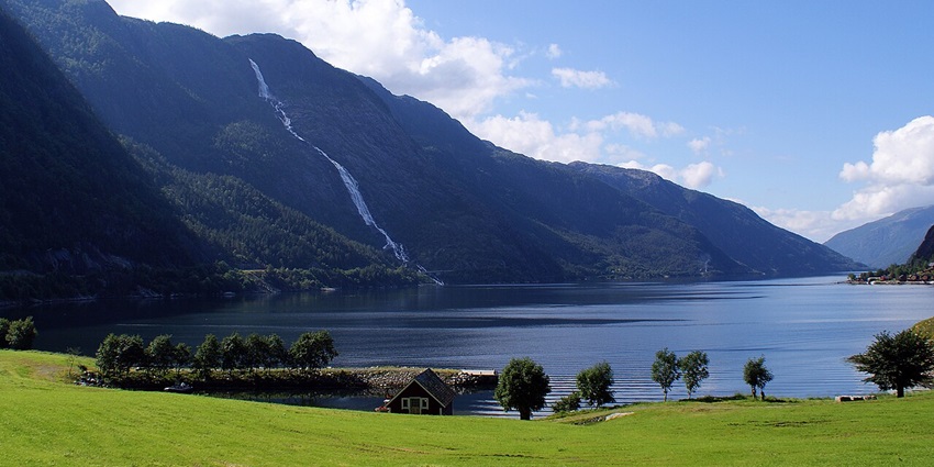 Åkrafjorden with distant buildings, a still water body of a lake, and surrounded by green hills, one of the hidden places in Norway.