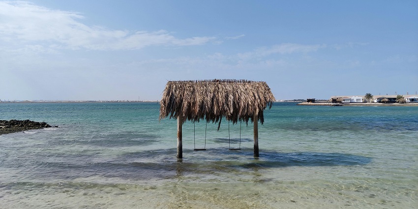 Swings hanging from a thatched roof on a sandy sea shore at Al Dar Islands, one of the peaceful islands in Bahrain.