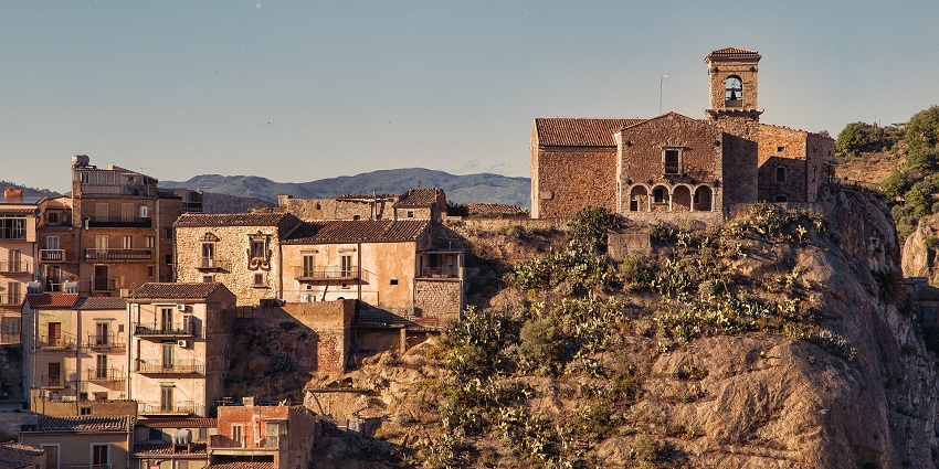 A cluster of stone buildings on a rugged mountain ridge with cliffs and terraces.