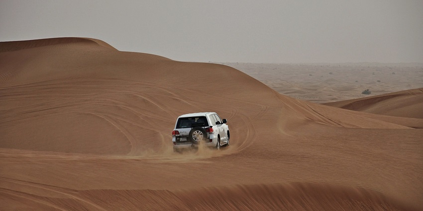 Vast Dubai desert landscape with undulating sand dunes under clear blue sky.