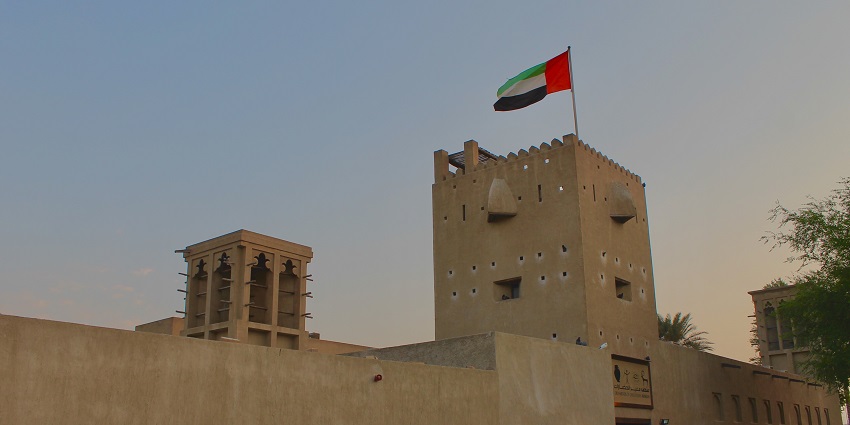 Al Shindagha Museum in Dubai with wind towers and the UAE flag atop a traditional building.