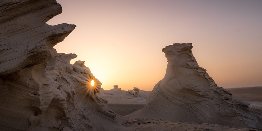 Al Wathba fossil dunes with unique formations of the sand and sun rising in the back.