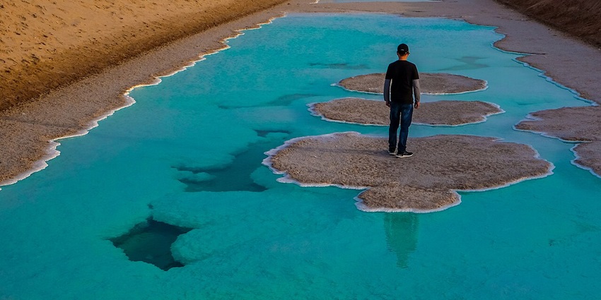 Al Wathba Salt Lake with clear blue water body of the lake and man standing on a surface.