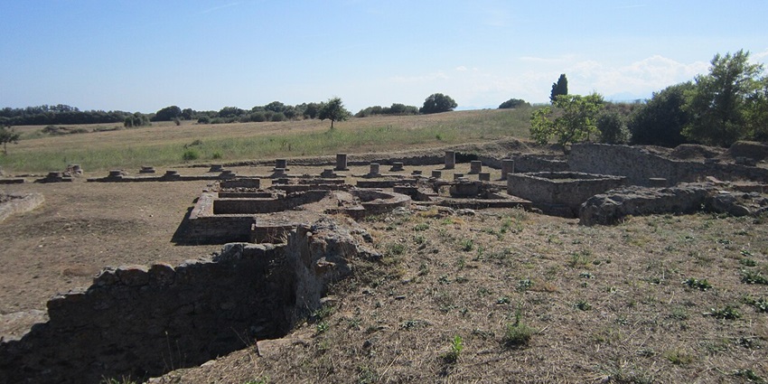 Aleria archaeological site with old ruined structures surrounded by green grass and plains.