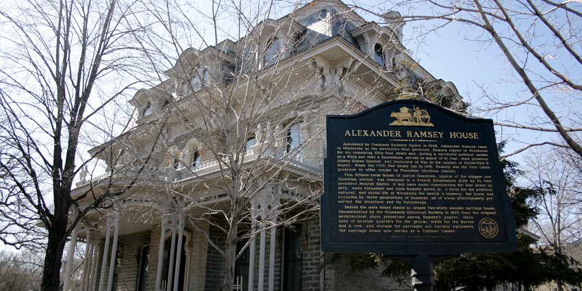Alexander Ramsey's house with white architecture, a black sign board and dried trees