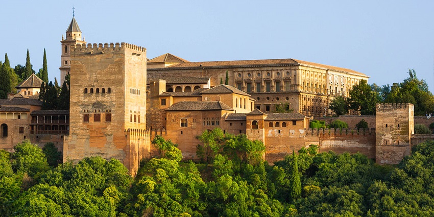 The Alhambra palace and fortress complex in Granada, surrounded by lush green trees.