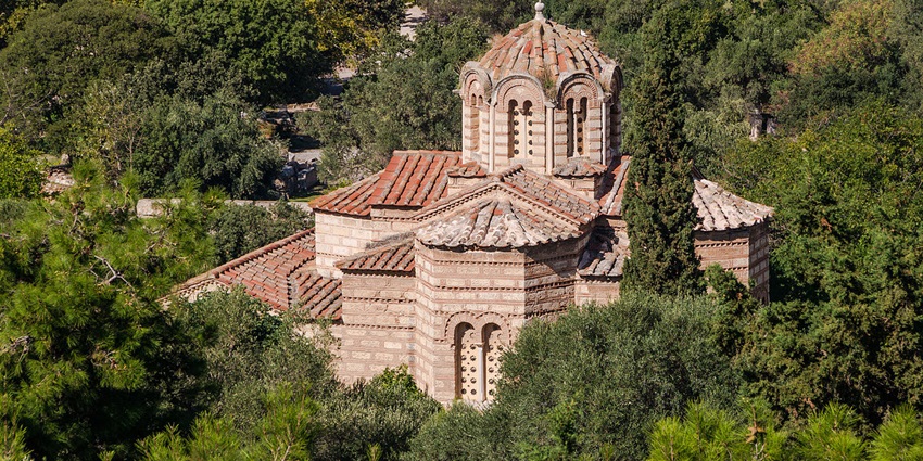 A small Byzantine-style church with a domed roof surrounded by dense green trees.