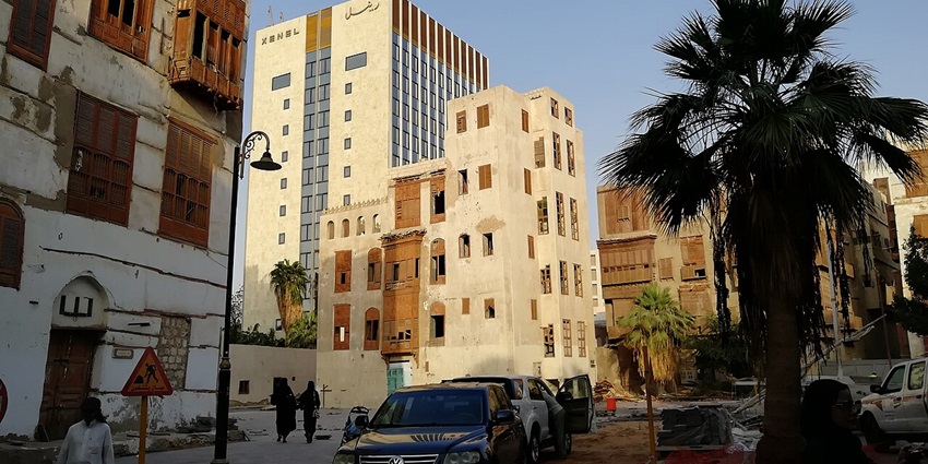 Old house in old Jeddah with multiple windows, street lamps, sign boards and vehicles parked