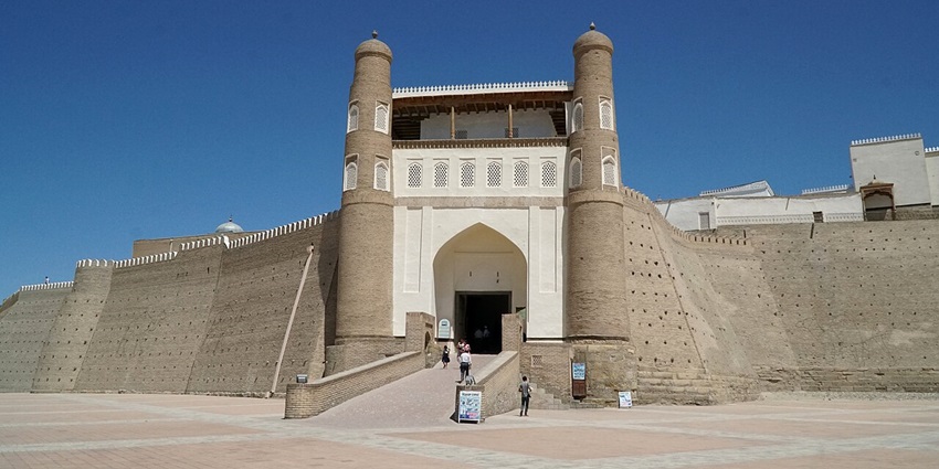 Entrance to the Ark of Bukhara with tall walls, people entering and traditional architecture
