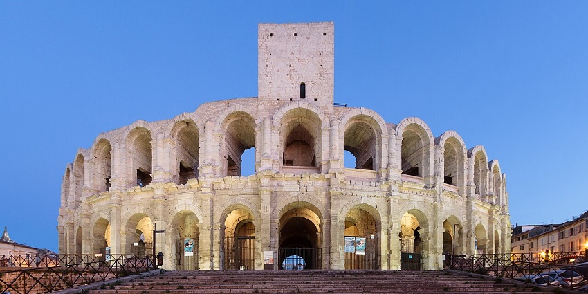 Ancient Roman amphitheatre with arched façade lit at twilight, historic landmark view, one of the historical places in France.