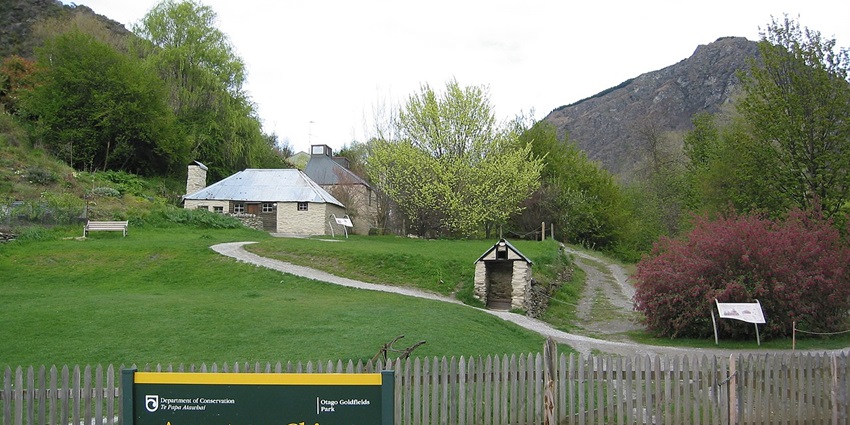 Entrance to the Arrowtown Chinese settlement with small buildings and a green signboard